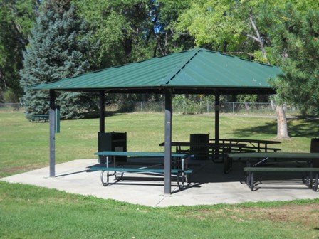 Benches under a shelter with a field and trees.
